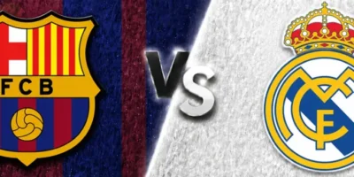 A wide sports matchup graphic featuring FC Barcelona and Real Madrid facing off. Barcelona’s crest appears on the left over a dark blue and maroon textured background with faint club imagery, while Real Madrid’s crest is on the right over a white textured background with a faded oversized logo watermark. A glowing diagonal divider separates the two sides, with large metallic “VS” text centered between the clubs. The design uses dramatic lighting, textured patterns, and soft gray borders above and below for a polished promotional look.
