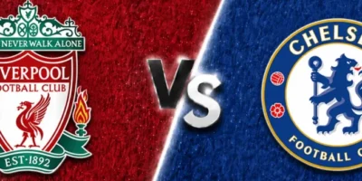 A wide sports matchup graphic featuring Liverpool and Chelsea facing off. Liverpool’s crest appears on the left over a textured deep red background with faint club imagery and branding, while Chelsea’s crest is displayed on the right over a textured royal blue background with a faded oversized club logo watermark. A glowing diagonal divider separates the two sides, with large metallic “VS” lettering centered between the clubs. The design uses dramatic lighting, textured patterns, and soft gray borders above and below for a polished promotional match graphic.