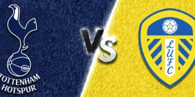 A wide sports matchup graphic featuring Tottenham Hotspur and Leeds United facing off. Tottenham’s crest appears on the left over a textured dark navy background with a faint oversized club watermark in the backdrop, while Leeds United’s crest is displayed on the right over a bright yellow textured background with faded club branding. A glowing diagonal divider separates the two sides, with large metallic “VS” lettering centered between the clubs. The design uses dramatic lighting, textured patterns, and soft gray borders above and below for a polished promotional match graphic.